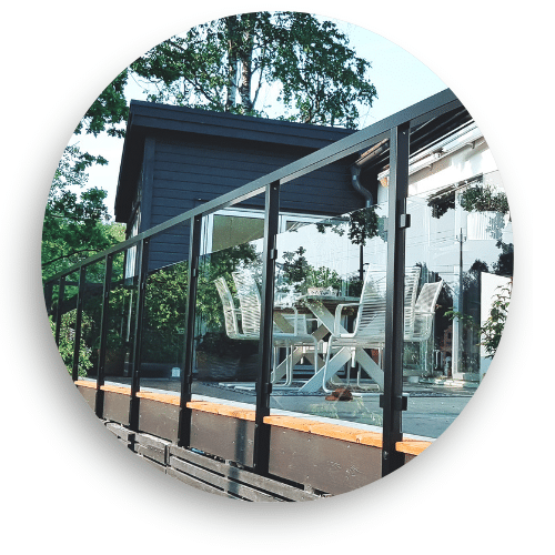 Glasgeländer mit schwarzen Alupfosten auf Terrasse – klare Scheiben und moderne Hausfassade mit Glasflächen im Hintergrund.