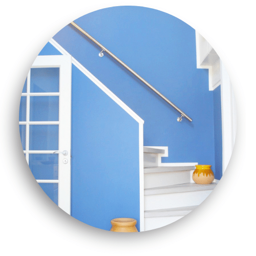 Wandmontierter Edelstahlhandlauf entlang einer blauen Treppenhauswand. Weiße Stufen und Kanten setzen einen eleganten Kontrast und schaffen ein modernes, funktionales Design.