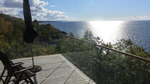 Eckmontiertes Glasgeländer mit Holzhandlauf und beeindruckendem Blick auf Meer und Wald von der Terrasse.