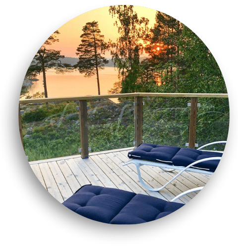 Glasgeländer mit Holzpfosten an Terrasse mit Seeblick – klare Scheiben, Sonnenuntergang, zwei dunkle Sonnenliegen.