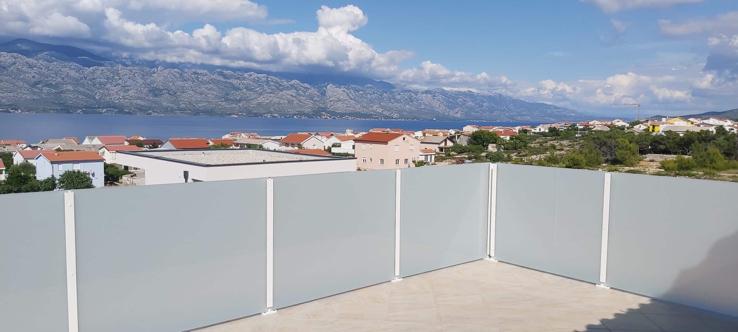 Balkon mit weißem, satiniertem Glasgeländer und Aluminiumpfosten – mit Blick auf Meer, Berglandschaft und Dächer in der Ferne
