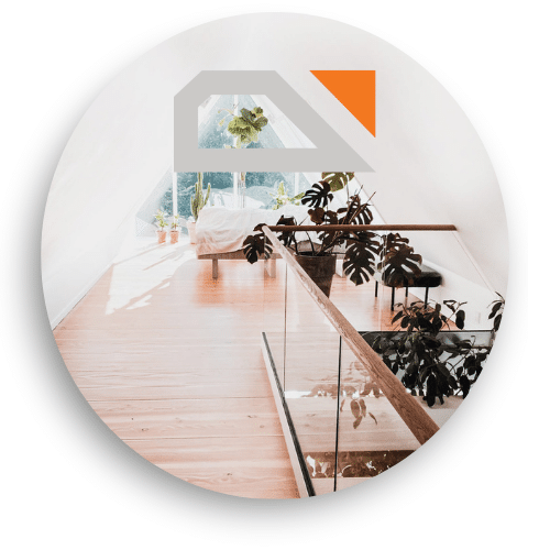 Glasgeländer mit Holzdetails entlang eines holzverkleideten Dachgeschosses. Große Fenster lassen Tageslicht herein, Pflanzen sorgen für eine helle, grüne Atmosphäre.