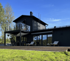 Modernes Glasgeländer mit schwarzen Pfosten und getöntem Glas auf einer oberen Holzterrasse, montiert an schwarzer Holzfassade eines Hauses.