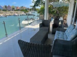 Glasgeländer mit Edelstahlpfosten, montiert an einer Terrasse mit Blick auf Bootskanal und farbenfrohe Häuser in tropischer Umgebung.