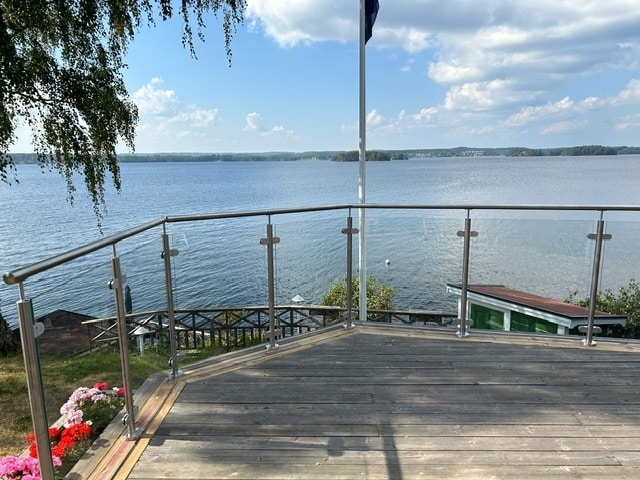 Glasgeländer mit runden Edelstahlpfosten auf einer erhöhten Terrasse mit Blick auf See und Holzsteg – modernes Design für freie Aussicht.