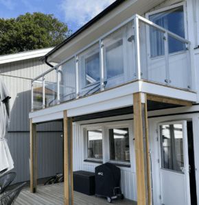 Balkon mit Glasgeländer und weißen Aluminiumpfosten in Holzoptik auf Holzdielen, Fassade in harmonischem Naturton.