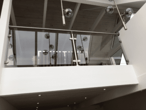 Loft mit Rauchglas-Geländer und Edelstahlhandlauf. Minimalistische Halterungen und moderne Beleuchtung spiegeln sich im Glas und unterstreichen das elegante Design.