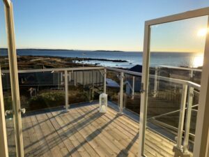 Balkon mit Glasgeländer und weißen Aluprofilen – geöffnete Türen mit Blick auf Meer und Schärenlandschaft.