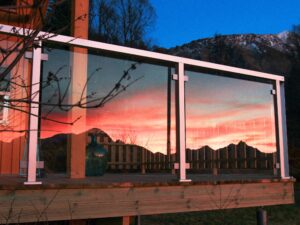 Glasgeländer mit weißem Rahmen auf Terrasse – intensive Farben des Sonnenuntergangs spiegeln sich im Glas.