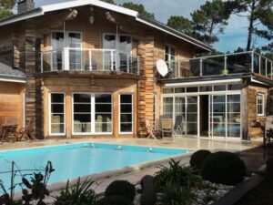 Glasgeländer rund um Balkon und Pool Getöntes Glasgeländer mit Edelstahlpfosten auf Balkon und Poolterrasse bei Blockhaus – umgeben von Kiefern und verglastem Außenbereich.